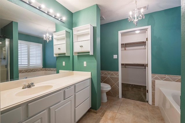 bathroom with tile walls, a tub to relax in, vanity, toilet, and an inviting chandelier