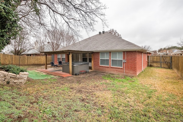 rear view of house featuring a hot tub, a patio, and a lawn