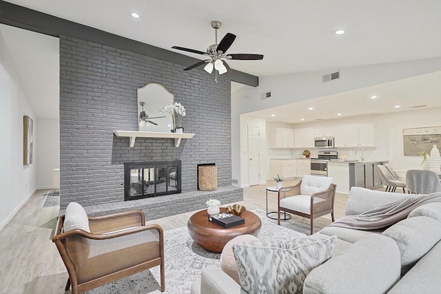 living room featuring vaulted ceiling, light wood-type flooring, ceiling fan, and a fireplace