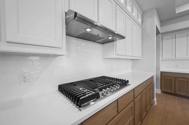 kitchen featuring white cabinetry, dark hardwood / wood-style flooring, stainless steel gas stovetop, range hood, and backsplash