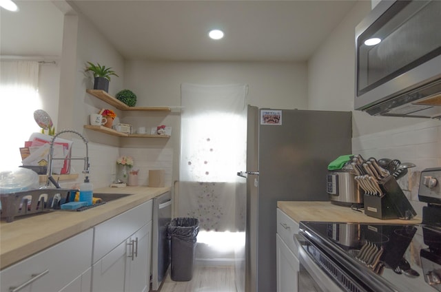 kitchen with tasteful backsplash, white cabinetry, sink, wooden counters, and stainless steel appliances