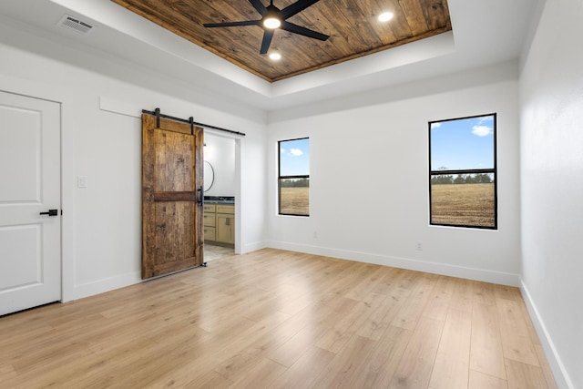 unfurnished bedroom featuring multiple windows, wood ceiling, light hardwood / wood-style floors, a raised ceiling, and a barn door