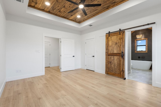 unfurnished bedroom with connected bathroom, a tray ceiling, a barn door, wooden ceiling, and light hardwood / wood-style flooring