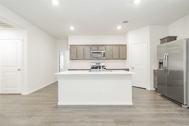 kitchen with appliances with stainless steel finishes, sink, a center island with sink, and light hardwood / wood-style flooring