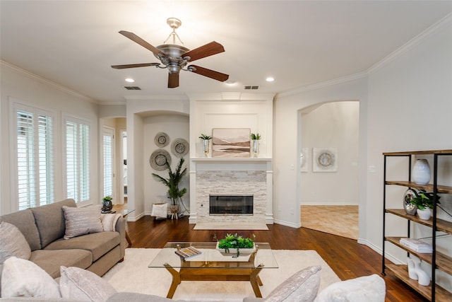 living room featuring dark wood-style floors, crown molding, and a stone fireplace