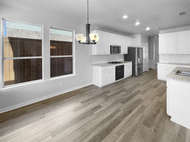 kitchen with appliances with stainless steel finishes, decorative light fixtures, white cabinets, hardwood / wood-style flooring, and a notable chandelier