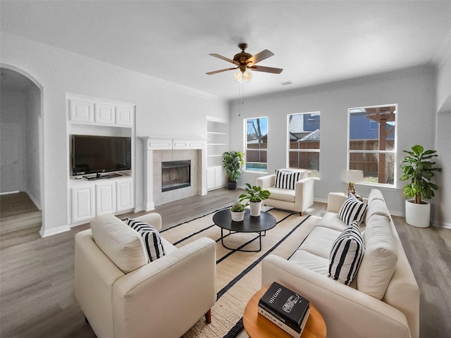 living room featuring ceiling fan, a fireplace, light hardwood / wood-style floors, and built in shelves