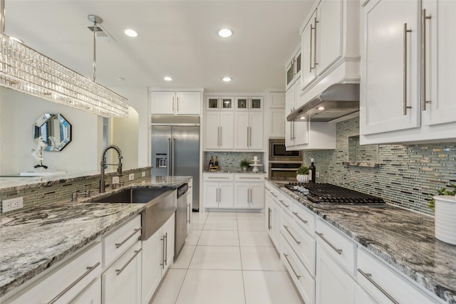 kitchen with sink, hanging light fixtures, built in appliances, white cabinets, and light tile patterned flooring