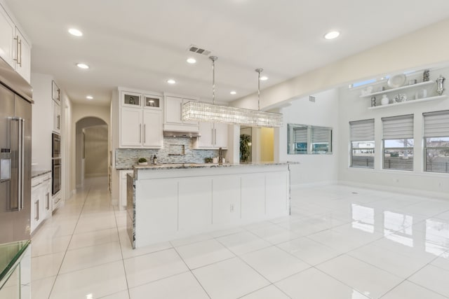 kitchen featuring appliances with stainless steel finishes, white cabinetry, an island with sink, decorative backsplash, and light stone countertops