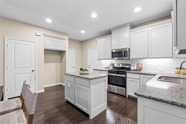 kitchen featuring sink, a center island, appliances with stainless steel finishes, light stone countertops, and white cabinets