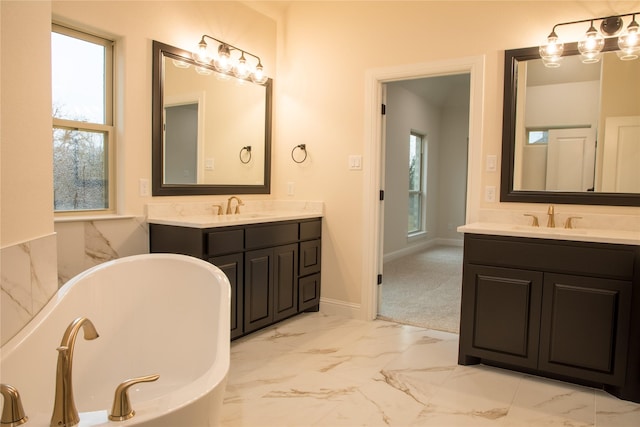 full bathroom featuring marble finish floor, two vanities, a soaking tub, and a sink