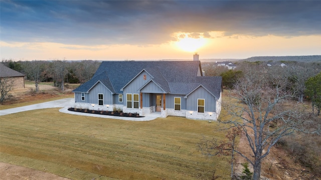 modern farmhouse with roof with shingles, a lawn, a chimney, and board and batten siding