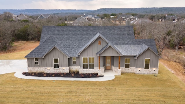 modern farmhouse style home with stone siding, a front lawn, roof with shingles, and board and batten siding