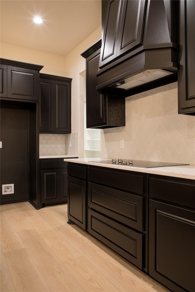 kitchen featuring light wood finished floors, decorative backsplash, custom exhaust hood, black electric cooktop, and light countertops