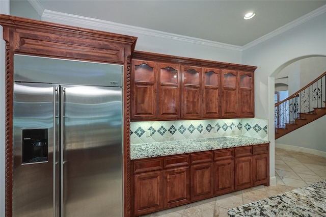 kitchen with light stone countertops, decorative backsplash, ornamental molding, and built in refrigerator