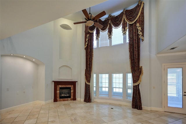 unfurnished living room with light tile patterned flooring, ceiling fan, a tiled fireplace, and a high ceiling