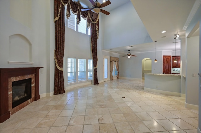 unfurnished living room with a wealth of natural light, a fireplace, ceiling fan, and a high ceiling