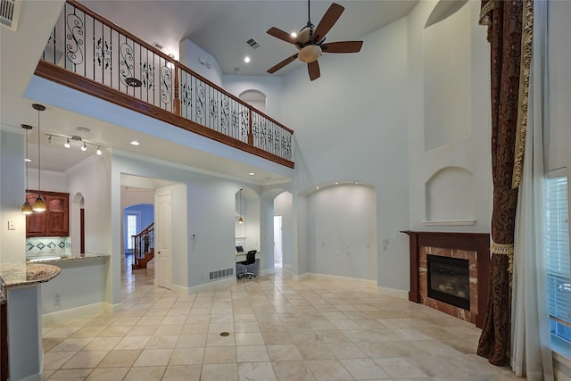 living room with light tile patterned floors, ornamental molding, ceiling fan, a tiled fireplace, and a high ceiling