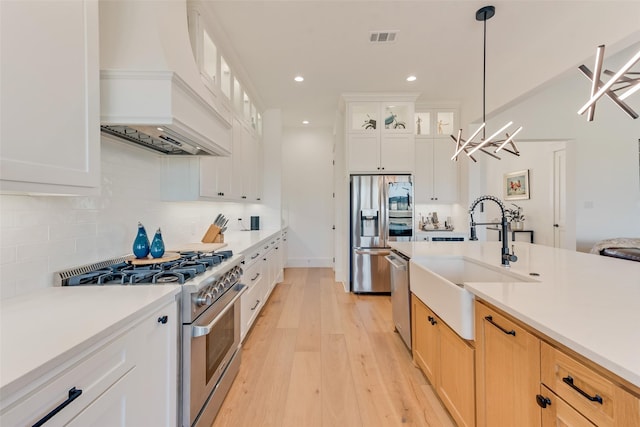 kitchen featuring stainless steel appliances, white cabinetry, hanging light fixtures, and custom range hood