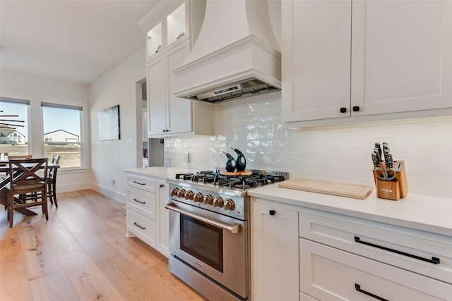 kitchen with premium range hood, high end stainless steel range, light hardwood / wood-style flooring, decorative backsplash, and white cabinets