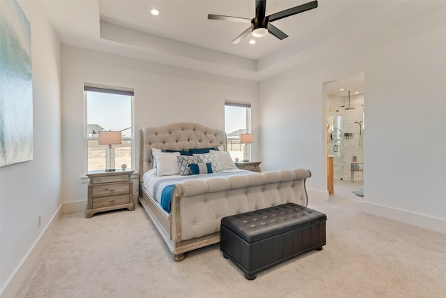 carpeted bedroom featuring multiple windows, a raised ceiling, and ensuite bathroom