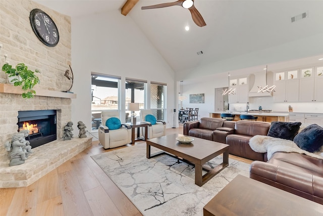 living room featuring beam ceiling, high vaulted ceiling, light wood-type flooring, ceiling fan, and a fireplace