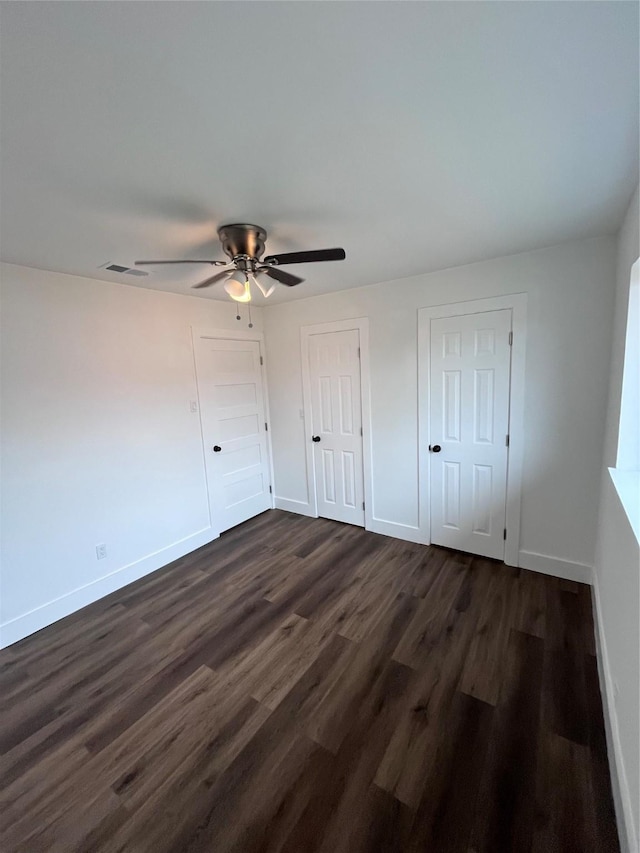 unfurnished bedroom featuring dark hardwood / wood-style flooring, two closets, and ceiling fan