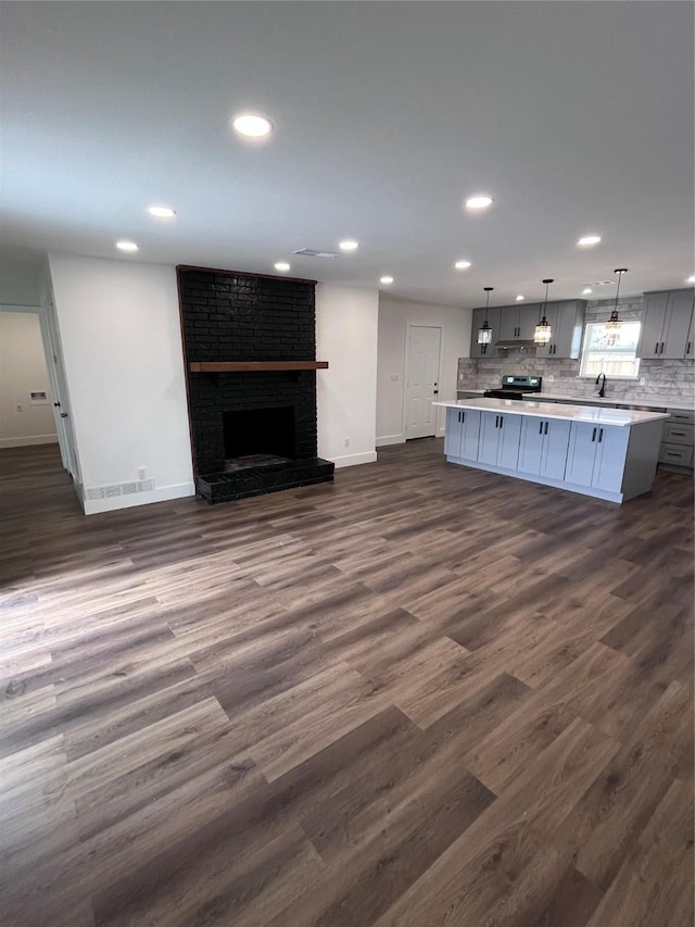 kitchen featuring dark wood-type flooring, stainless steel range with electric stovetop, a center island, pendant lighting, and decorative backsplash