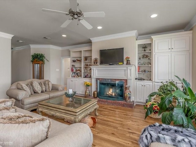 living room featuring built in shelves, crown molding, ceiling fan, a fireplace, and light hardwood / wood-style floors