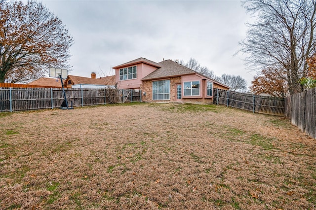 back of house featuring a fenced backyard, a lawn, and brick siding