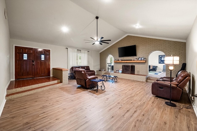 living room featuring vaulted ceiling, brick wall, ceiling fan, light hardwood / wood-style floors, and a brick fireplace