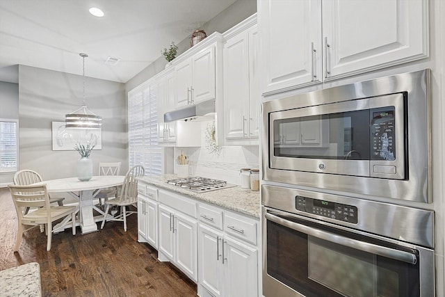 kitchen with appliances with stainless steel finishes, dark hardwood / wood-style floors, light stone countertops, white cabinets, and decorative light fixtures