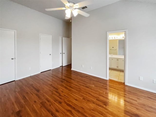 unfurnished bedroom featuring connected bathroom, hardwood / wood-style floors, two closets, and ceiling fan