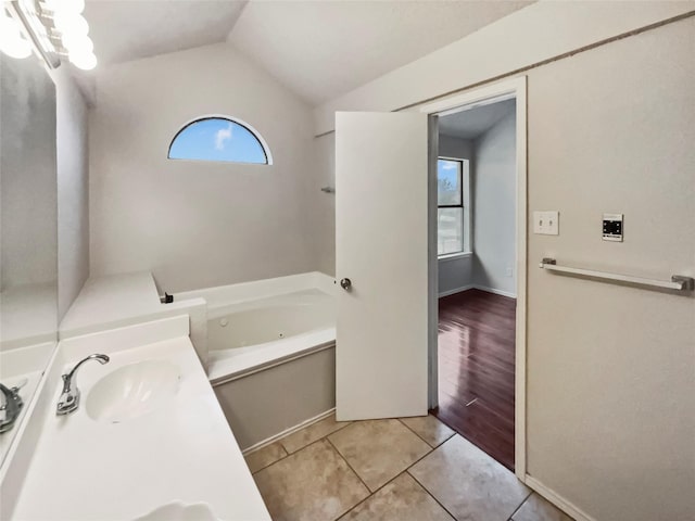 bathroom with tile patterned flooring, plenty of natural light, lofted ceiling, and a tub to relax in