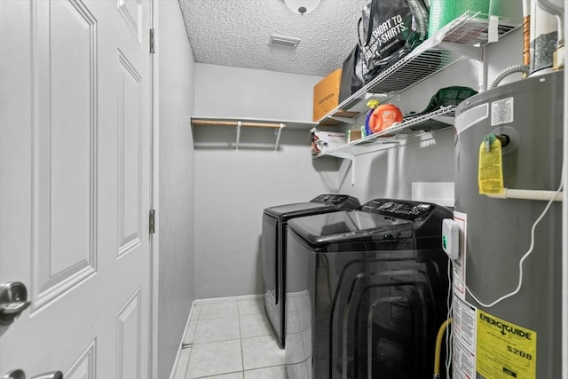 clothes washing area featuring water heater, light tile patterned floors, a textured ceiling, and independent washer and dryer