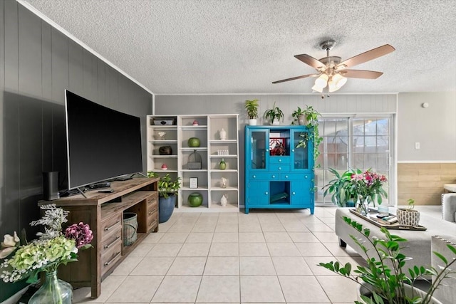 living room featuring a textured ceiling, light tile patterned floors, ornamental molding, wooden walls, and ceiling fan