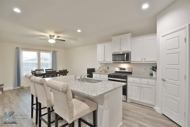 kitchen with appliances with stainless steel finishes, sink, white cabinets, light stone counters, and a center island with sink