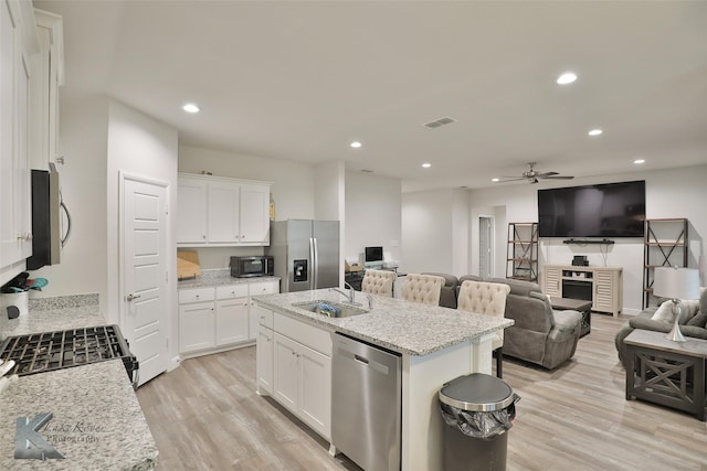 kitchen with a kitchen island with sink, light stone countertops, white cabinets, and appliances with stainless steel finishes