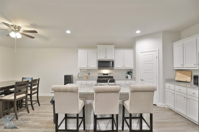 kitchen with white cabinetry, a breakfast bar area, a kitchen island with sink, light stone counters, and stainless steel appliances