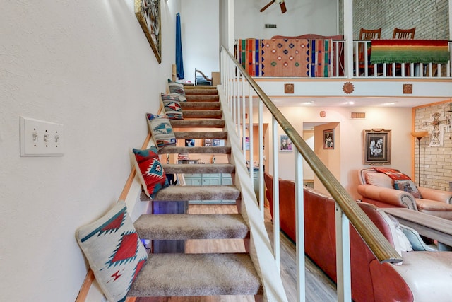 staircase featuring a towering ceiling, visible vents, and wood finished floors