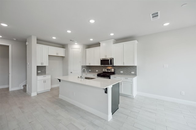 kitchen with sink, appliances with stainless steel finishes, a kitchen island with sink, white cabinets, and decorative backsplash