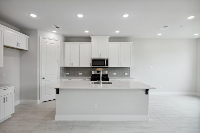 kitchen with white cabinetry, stainless steel appliances, and a center island with sink