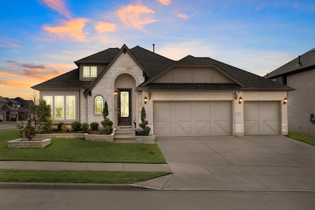 french country style house with driveway, roof with shingles, a front lawn, stone siding, and a garage