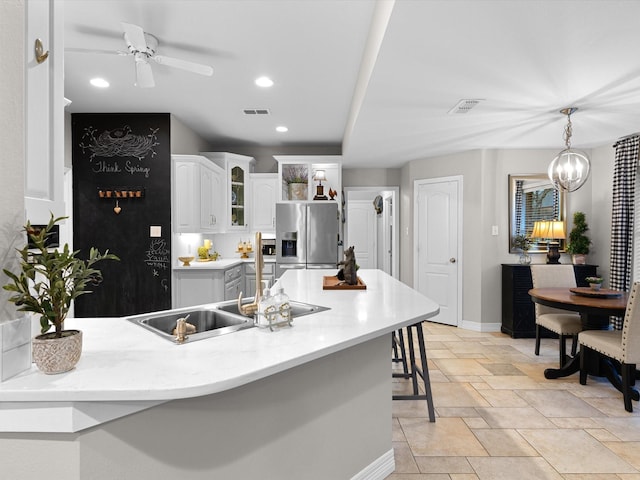 kitchen featuring sink, white cabinetry, stainless steel refrigerator with ice dispenser, a kitchen bar, and decorative light fixtures