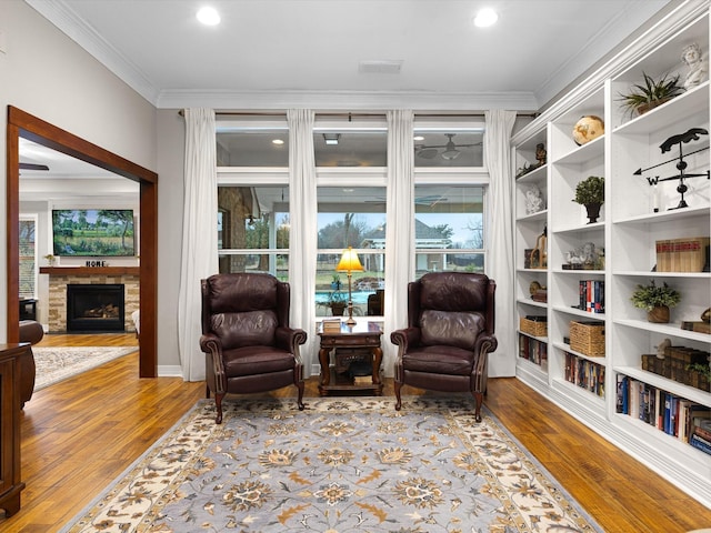 living area with a stone fireplace, light hardwood / wood-style flooring, and ornamental molding