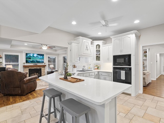 kitchen with sink, white cabinetry, black appliances, a kitchen bar, and kitchen peninsula