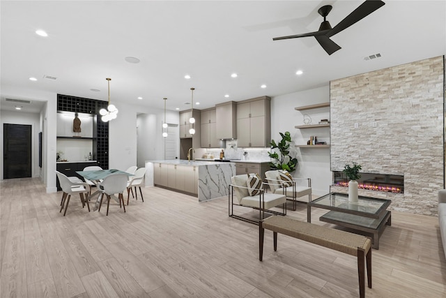 living room featuring ceiling fan, sink, a fireplace, and light hardwood / wood-style floors