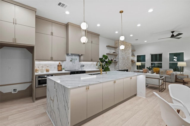 kitchen with sink, light hardwood / wood-style floors, an island with sink, and stainless steel oven