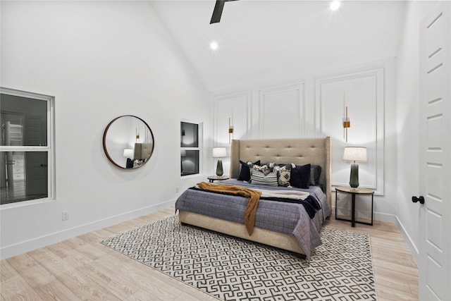 bedroom with ceiling fan, high vaulted ceiling, and light hardwood / wood-style flooring