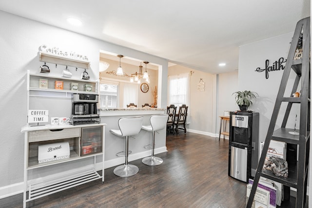 kitchen with dark wood-type flooring, a breakfast bar area, kitchen peninsula, and hanging light fixtures